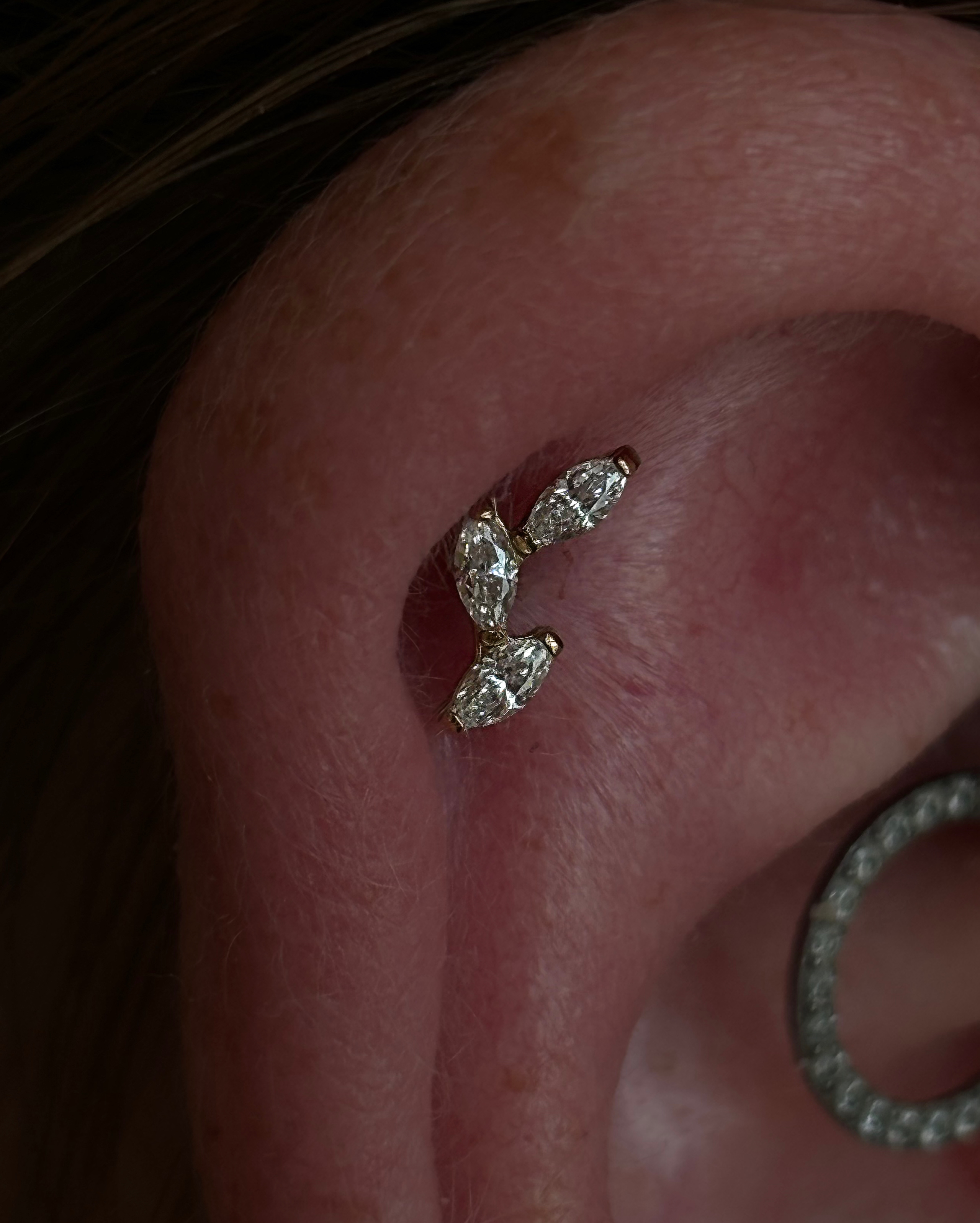 Extreme close-up of daith with 4-marquise-stone curved barbell and crystal huggie hoop lobe