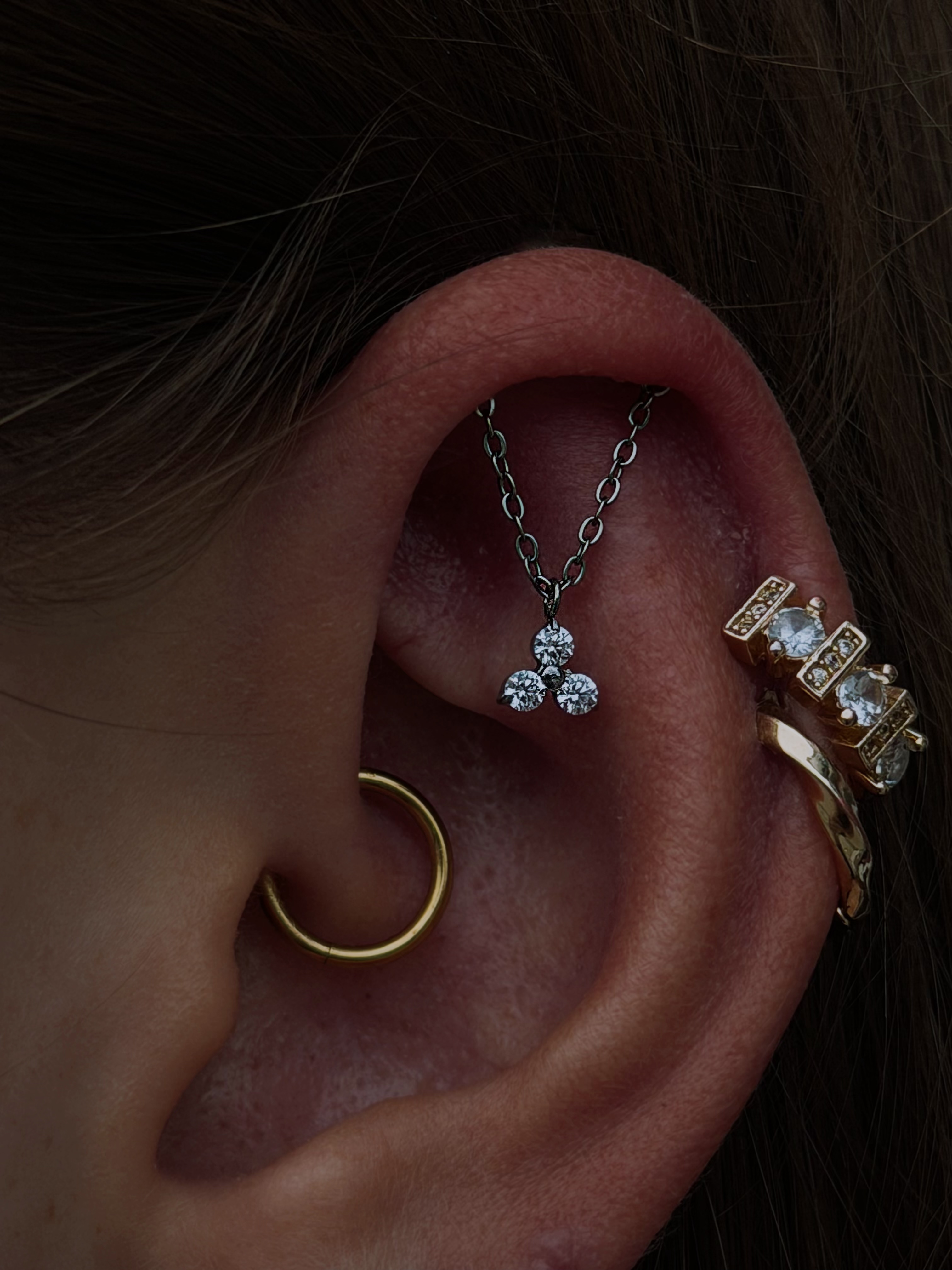 Curated ear with gold tragus hoop, helix chain jewelry, and crystal studs